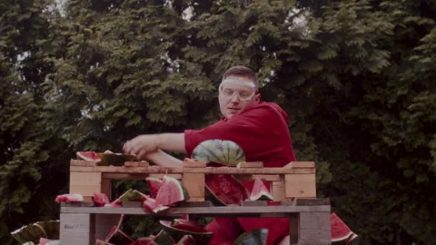 A Man in a red coat slicing some watermelons during the day 스톡 동영상 258308141