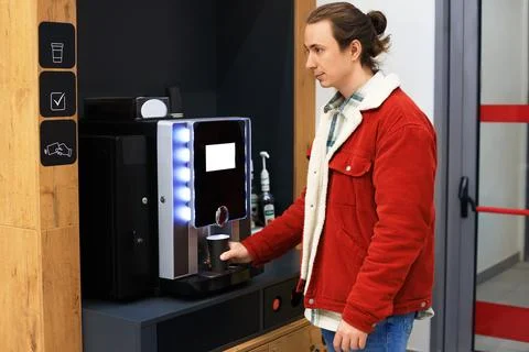 Man in a red corduroy jacket using a modern, self-service coffee machine to.. Stock Photos
