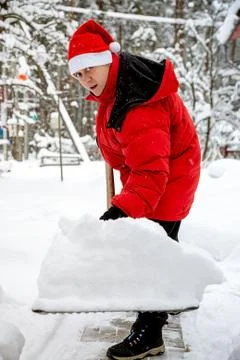 Man in red down jacket and red hat of Santa claus clears snow in backyard. Cl Stock Photos