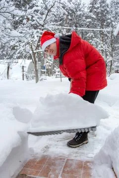 Man in red down jacket and red hat of Santa claus clears snow in backyard. Cl Foto stock