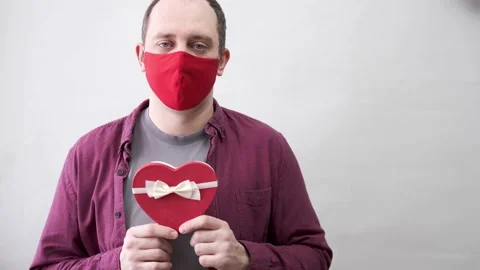 Man in red face mask holding red heart gift box. Valentine day gift Stock Footage 146120575