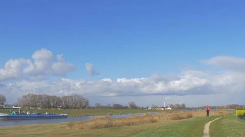 Man in Red Far From Camera Backpacker is Walking Along a River by Meadow Video stock 60860363