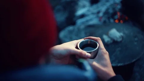 A man in a red hat is holding a mug of tea in the nature by the fire. Stock Footage