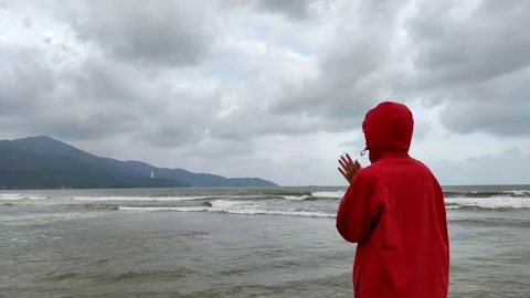 Man in red hoodie in a cold cloudy day by the wavy blue sea Stock Footage 146251304