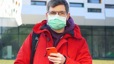 Man in red jacket and glasses with sterile mask on the street and holding phone Stock Footage 129940322