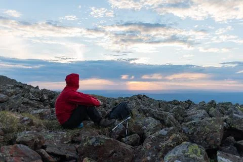 A man in a red jacket with a backpack and trekking poles enjoying the sunset  Stock Photos