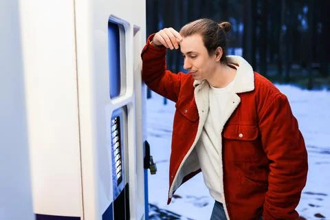Man in red jacket choosing snack from vending machine in winter park. Foto stock