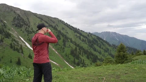 Man in red jacket enjoys beverage while overlooking green mountain landscape Video stock 340391976