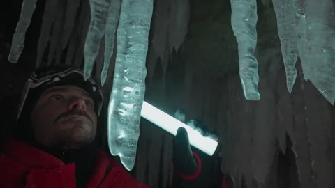 Man in red jacket with led light illuminate a lot of frozen icicles in ice cave Stock Footage 166567298