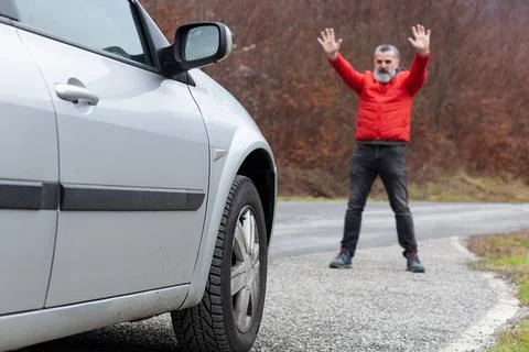 Man in red jacket on mountain road gesturing to car to stop Stock Photos
