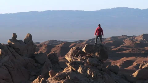 Man in red jacket standing atop rocky mountain with sky in background Stock-Footage 274531974