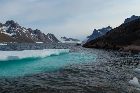 Man in red jacket standing in black inflatable boat near iceberg in Greenland Stock Photos