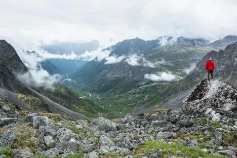 Man in red jacket standing on boulder overlooking glacially carved valley in Stock Photos