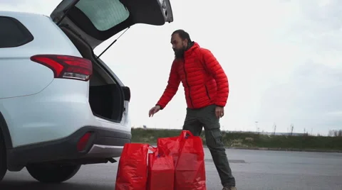 Man in red jacket taking shopping bags with purchases out from the trunk Stock Footage 67673948