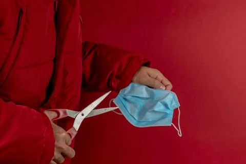 Man in red jacket trying to cut a protective mask in half against corona viru Stock Photos