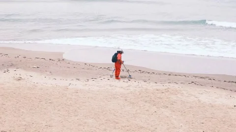Man in red jumpsuit looking for lost luxuries with electronic metal detector on Stock-Footage 168504118