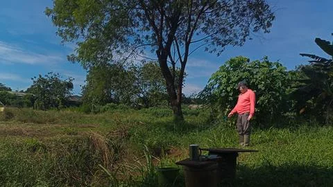 A man in red is relaxing on the edge of a watering hole while fishing Stock Photos