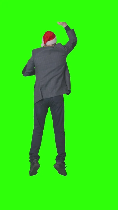 A man in a red Santa hat dances energetically and waves his arms against a green Stock Footage 330076675