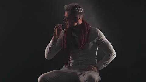Man in a red scarf sits and smokes an electronic cigarette Stock Footage 121483047