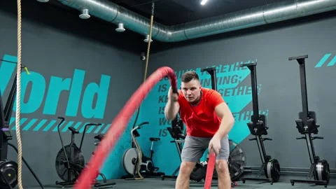 Man in red shirt pulling red rope in modern gym. Boxer doing some cross training Stock Footage 272324368
