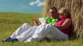 Man with red smartphone and woman with tablet computer sits near a haystack HD Footage