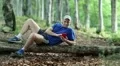 Man with red smartphone lies on a fallen tree in the forest HD Footage