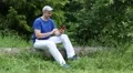 Man with red smartphone sits on a fallen tree in the forest HD Footage
