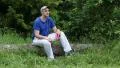 Man with red smartphone sits on a fallen tree in forest and listens to music HD Footage