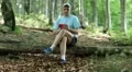 Man with red smartphone sits on a fallen tree in the forest HD Footage