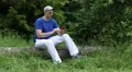 Man with red smartphone sits on a fallen tree in the forest HD Footage