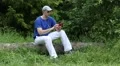 Man with red smartphone sits on a fallen tree in the forest HD Footage
