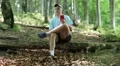 Man with red smartphone sits on a fallen tree in forest and listens to music HD Footage