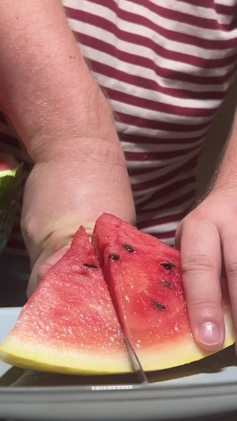 Man in red striped vest cuts fresh juicy red raw sweet watermelon on grey plate Vídeo Stock 280482895