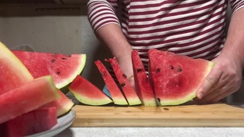 Man in red striped vest cuts watermelon on wooden cutting board Vídeo Stock 293618082