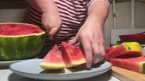 Man in red striped vest cuts ripe tasty red raw sweet watermelon on gray plate Stock Footage 297206985