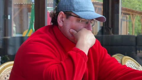A man in a red sweatshirt is sitting at a table in a cozy café, attentively read Stock Footage 310838371