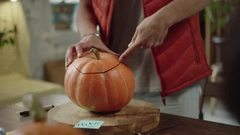 A man in red vest is cutting the top of the halloween pumpkin Stock Footage 170270325