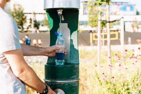 Man refilling plastic water bottle at public drinking fountain in city park Stock Photos