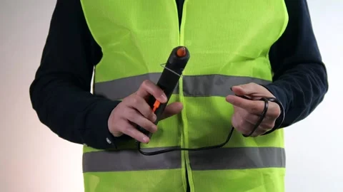 A man in a reflective construction vest holds a tool in his hands and checks its Stock Footage 313189701