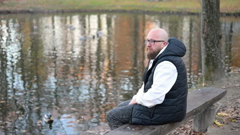 Man reflects by tranquil pond surrounded by autumn trees and gentle ripples in Stock Footage 346546341