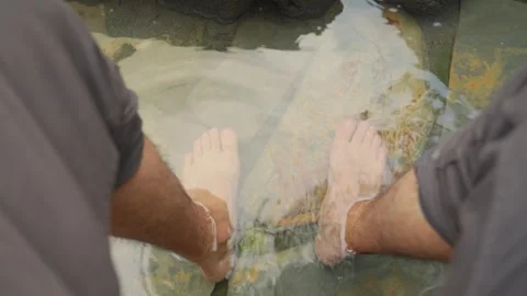 Man refreshing feet in a clear water pool on a rocky beach Stock Footage 340920879