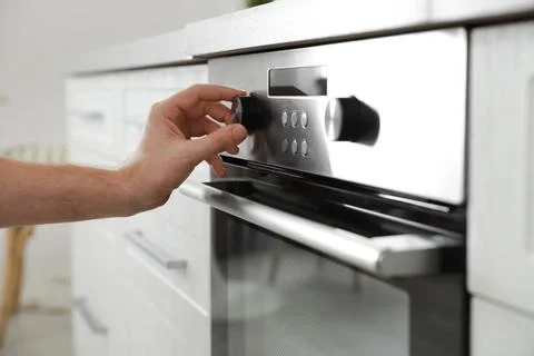 Man regulating cooking mode on oven panel in kitchen, closeup Stockfoto's