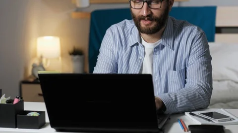 Man rejoices at end of project. Bearded guy sitting at desk in bedroom typing on Stock Footage 129383606