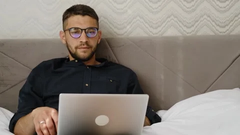 Man relaxes after finishing remote work on laptop while lying in bed at home Stock Footage 342543900