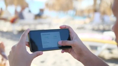 A man relaxes on the beach while using his phone to monitor his fitness progress Vídeo Stock 318408173