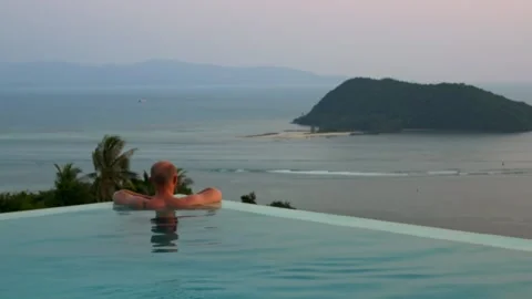 Man relaxes in infinity pool overlooking tropical island and ocean. Scenic view Stock-Footage 288376059