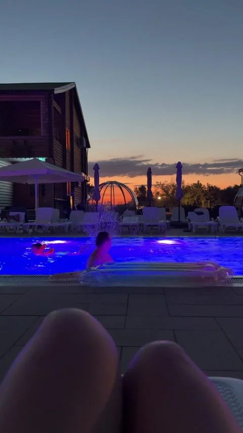 Man relaxes on an inflatable float in a glowing resort pool at sunset. A wooden Stock Footage 348168442
