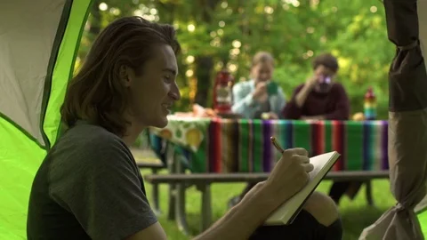 Man Relaxes Inside Tent, Writes In Journal, Chats With Friends At Picnic Table Video stock 77879201