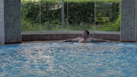 A man relaxes in the Jacuzzi pool at the spa resort, enjoying a luxurious life Stock Footage 80048109