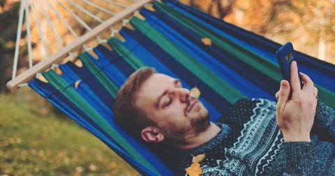 Man Relaxes, Uses Smartphone in a Hammock in Autumn. SLOW MOTION. 스톡 동영상 140295621